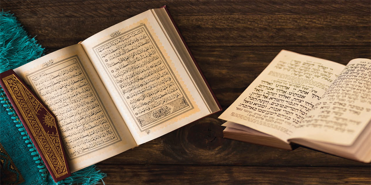 An open Qur’an and an open Torah resting side by side on a wooden table
